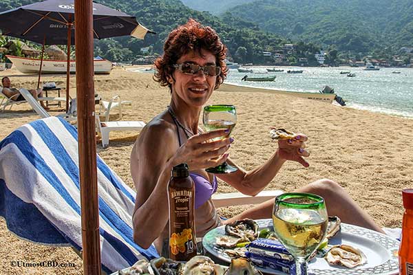 A woman is drinking wine and eating oysters on a beach while taking her sunbath