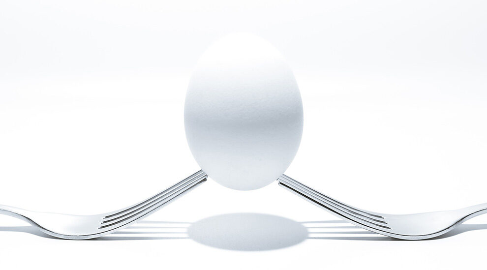 A white egg balanced on 2 forks